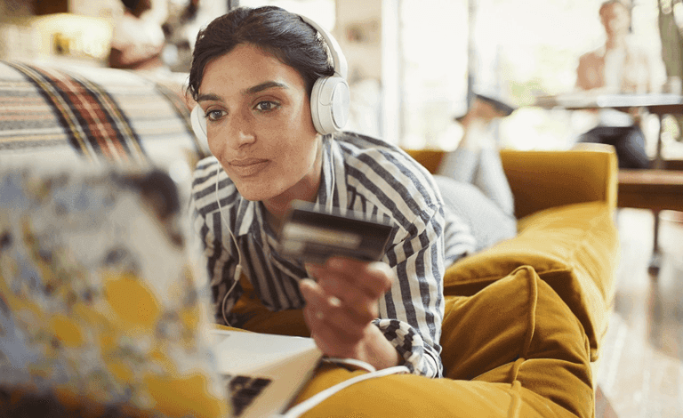Woman lying on a couch with a bank card and laptop
