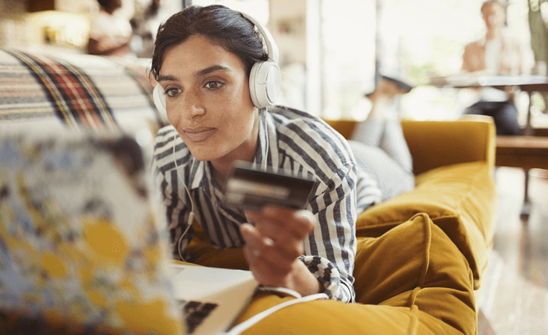 Woman lying on a couch with a bank card and laptop